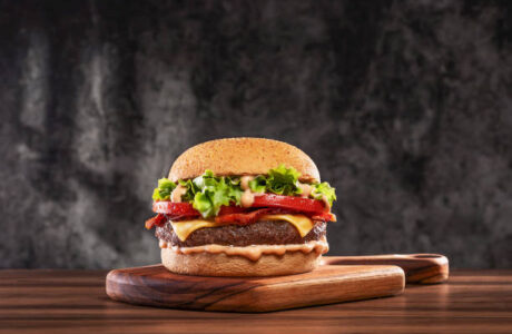 Cheeseburger with tomato and lettuce on wooden plank